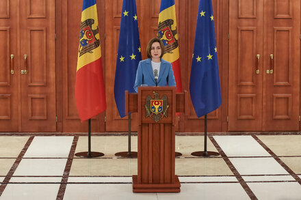 A woman casts her ballot at a polling station in Moldova. She holds an identity document while a ballot is visible on the table. The background is slightly blurred.