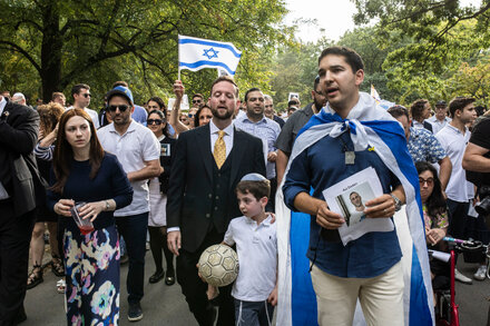 A diverse crowd of New Yorkers gathers, holding signs and candles, at an event commemorating the Oct. 7 anniversary, with a focus on peace talks.