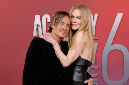 Nicole Kidman y Keith Urban caminando por una alfombra roja, sonriendo y tomados de la mano, con Nicole vistiendo un vestido dorado brillante y Keith un traje oscuro.