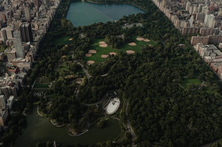 An aerial view of New York City showcasing a park with lush green trees amidst skyscrapers, suggesting a hidden green oasis.