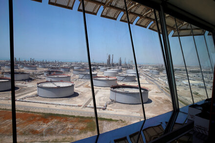 Leaders from OPEC Plus countries gathered around a large table, shaking hands and smiling, with oil rigs visible in the background.