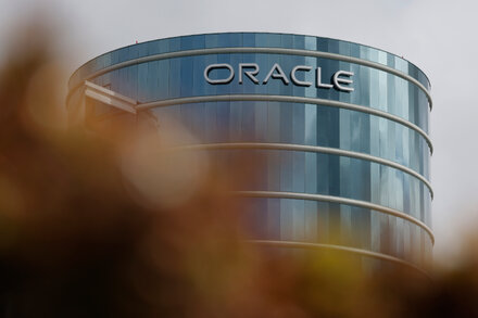 A person looking at a digital display showing stock market data, with various tech company logos including Oracle, symbolizing AI investment and market volatility.
