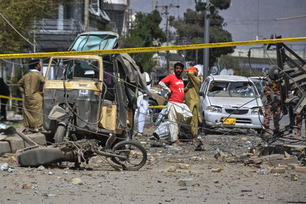 Rescue workers and residents gather at the scene of a car bomb explosion in Balochistan, Pakistan, with debris scattered around and damaged vehicles visible.