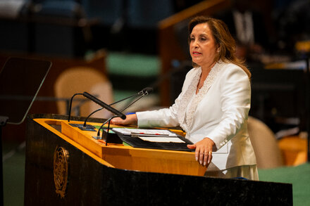 Peruvian President Dina Boluarte looking serious, addressing the public after her impeachment vote, with a flag visible in the background.