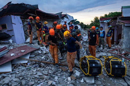 Rescuers search through rubble in the Philippines after a deadly earthquake, with debris and damaged structures visible.