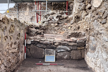 Archaeologists excavate a preserved skeleton in the ruins of Pompeii, with Mount Vesuvius in the background.