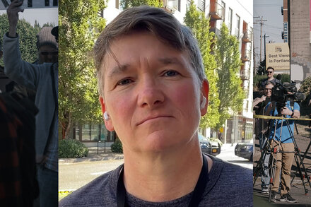 Federal officers standing in front of the Portland federal courthouse building, facing protesters. The courthouse is boarded up and spray-painted with graffiti. Smoke fills the air.