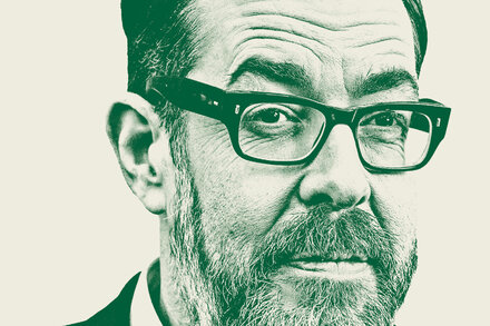 Richard Osman, author of 'The Thursday Murder Club' series, smiles while looking directly at the camera. He is wearing a dark jacket over a lighter shirt. The background is softly blurred.