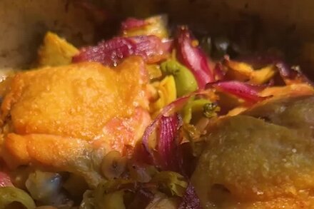 A close-up of a plate of spicy vinegar chicken over artichokes, garnished with fresh herbs.