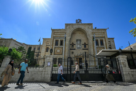 A woman casts her vote in a parliamentary election in Syria, with other voters and officials in the background.