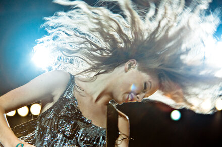 Taylor Swift performing on stage with a guitar and microphone, bathed in bright lights, during a concert early in her career.