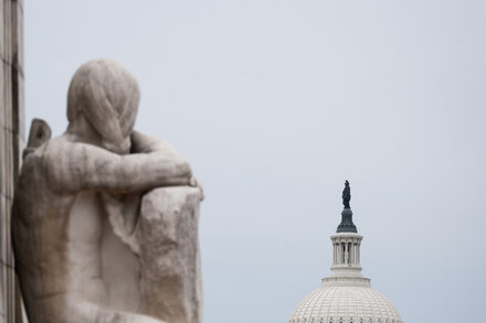 A wide shot of the United States Capitol building under a cloudy sky, with a sense of unease or tension in the atmosphere, reflecting a government shutdown.
