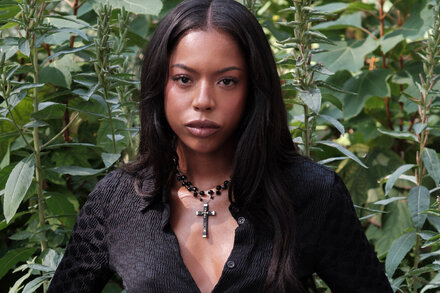 True Whitaker wearing a large, ornate silver necklace with a central gemstone, looking contemplative.