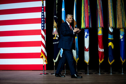 Donald Trump speaking to an audience of military generals and admirals, holding a microphone.