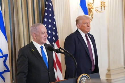 Donald Trump with a serious expression, gesturing while speaking at a podium with microphones, relevant to his Gaza plan.