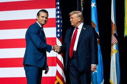 Donald Trump and Pete Hegseth at Quantico, surrounded by military personnel, with a focus on their campaign event.