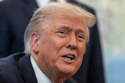 Donald Trump speaks at a podium, with an American flag visible in the background.