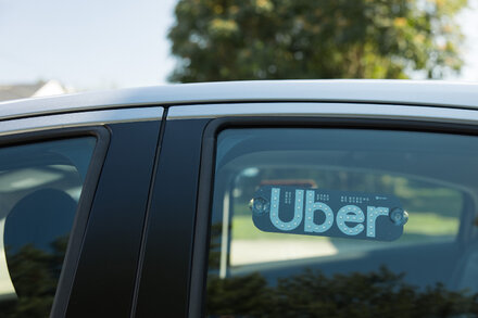 Close-up of the Uber app logo on a smartphone screen, with a blurred background suggesting a city street at night.