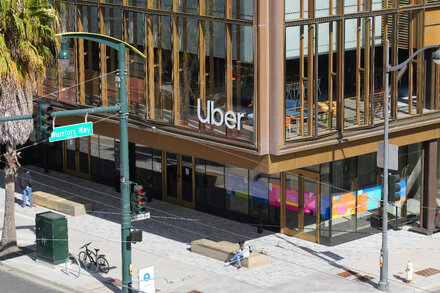 A woman stands in front of a modern glass building, looking concerned. The image relates to a jury finding Uber not responsible for sex assault, as more cases emerge.