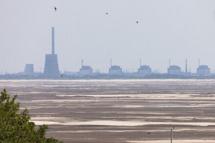 Damaged power lines and buildings surrounding the Zaporizhzhia Nuclear Power Plant, with smoke or steam rising in the distance.