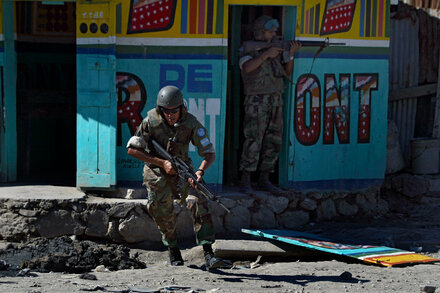 A U.N. peacekeeper stands guard in Haiti, with local citizens in the background, during a mission to combat gang violence.