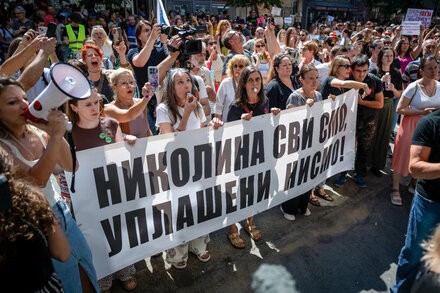 A woman stands in a protest crowd, her face showing determination. The image is a close-up, focusing on her expression amidst a blurred background of other protesters and signs. It evokes a sense of civic engagement and a fight for rights.
